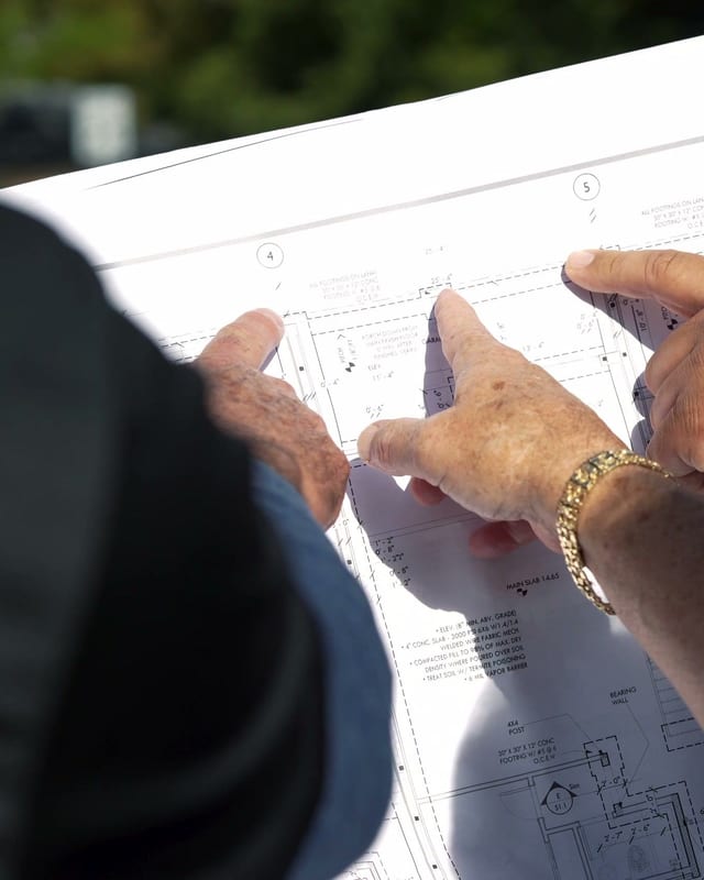 Two A Squared Roofing team members leaning over architectural drawings at a jobsite, pointing out details on the foundation plan.